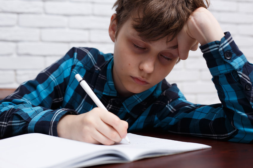 A boy dozing off while writing on a book